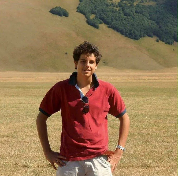 Carlo Acutis con camiseta polo roja en un campo abierto