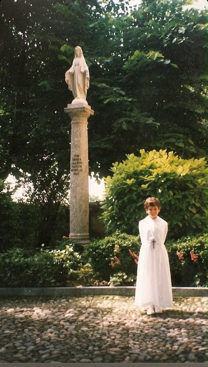 San Carlo Acutis de niño, vestido de blanco, junto a una imagen de la Virgen